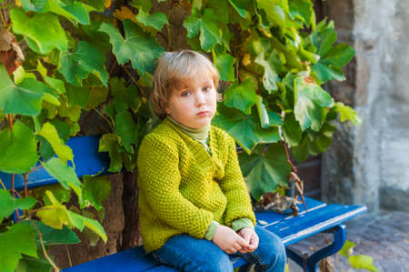 Sad toddler boy sitting on a bench outdoorsの写真素材