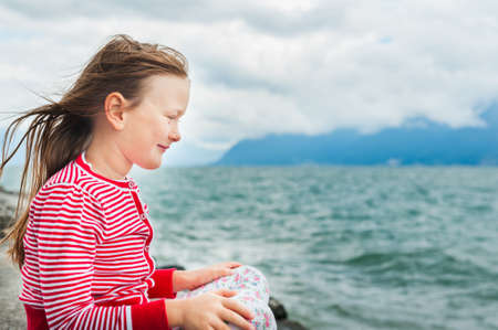 Adorable little girl resting by the lake on a very windy dayの写真素材