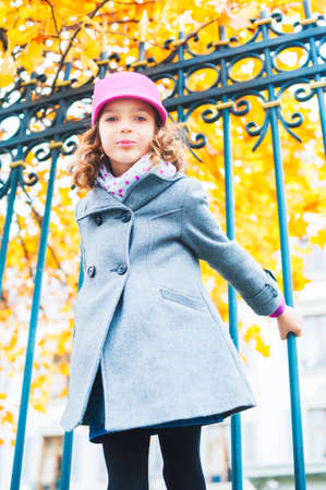 Lovely little girl playing outdoors, wearing grey coat and pink hatの写真素材