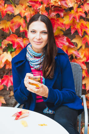 Outdoor portrait of a beautiful woman with a cup of comamile tea in autumn gardenの写真素材