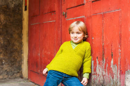 Outdoor portrait of adorable toddler boy, wearing bright green knit pullover, standing next to red doorの写真素材