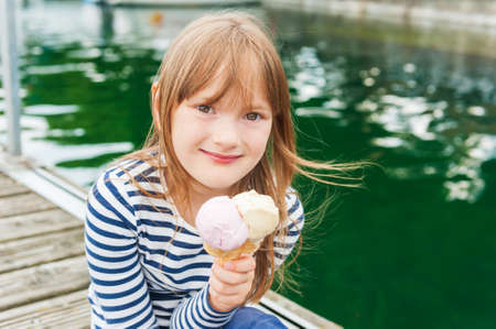 Outdoor portrait of a cute little girl, eating ice cream in a portの写真素材