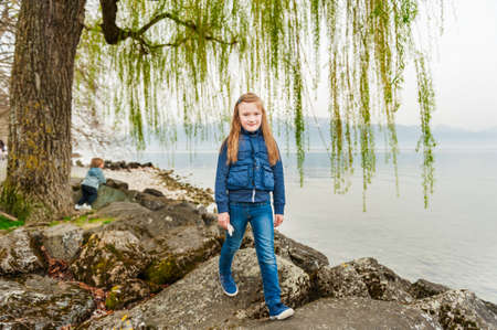 Cute little girl playing next to beautiful lake in early springの写真素材