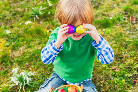 Adorable little blond boy playing with colorful easter eggs in the parkの写真素材