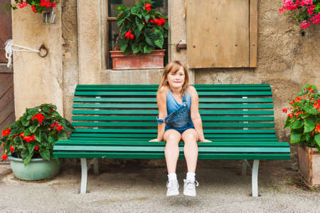 Summer portrait of a cute little girl of seven years old sitting on the bench in the yardの写真素材