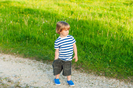 Cute toddler boy playing outdoor on a nice sunny evening, wearing shorts, white and blue top and...