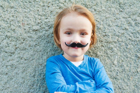 Outdoor close up portrait of a cute little boy with fake italian moustacheの写真素材