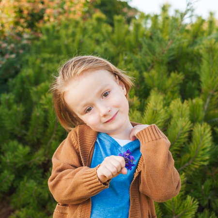 Outdoor portrait of a cute little boy of 4 years old, holding first spring flowers violetsの写真素材