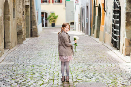Outdoor portrait of a cute little girl with bouquet of white roses, looking back over her shoulderの写真素材