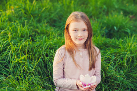 Outdoor portrait of a cute little girl on sunset, playing in the park with big magnolia flowerの写真素材