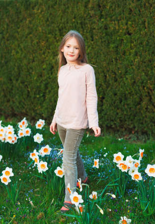 Cute little girl of 7 years old playing in the spring park between daffodils flowersの写真素材