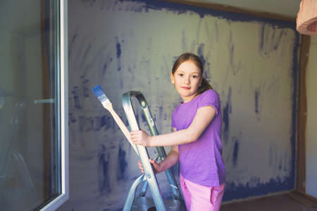 Cute little girl sitting on a step ladder, holding a brush. Renovation conceptの写真素材
