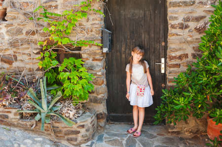 Summer portrait of a cute little girl, standing next to old wooden doorの写真素材