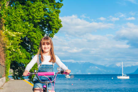 Cute little girl riding on a bicycle by the lakeの写真素材