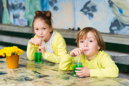 Two cute kids drinking green mint syrup in a cafeの写真素材