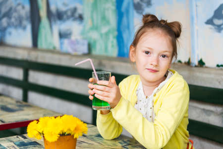 Adorable little girl drinking mint syrup in a cafe, wearing yellow jacketの写真素材