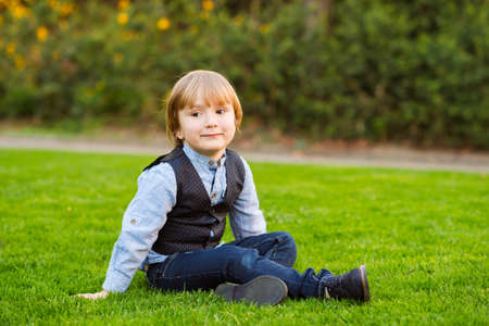 Outdoor portrait of adorable little boy of 4 years old sitting on a lawn in the park at sunsetの写真素材