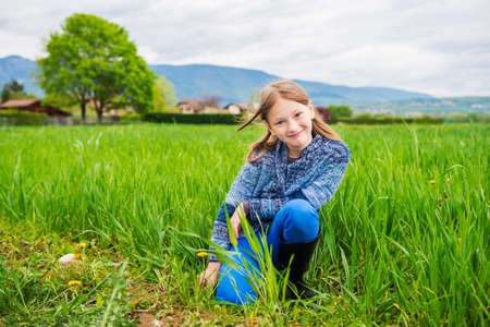 Fashion portrait of cute little girl of 7 years old wearing blue trousers knitted jacket and black rain bootsの写真素材