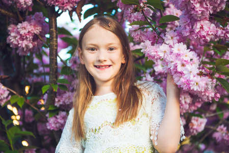 Outdoor spring portrait of a pretty little girl standing between flowers of a japanese cherry in blossomの写真素材