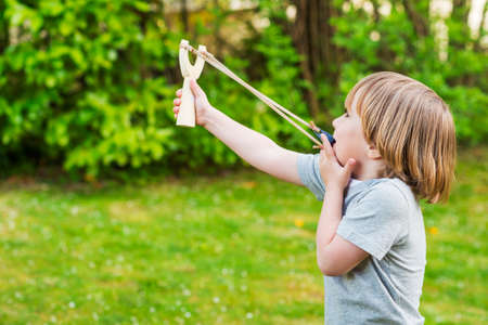 Cute little boy playing with slingshot outdoorsの写真素材