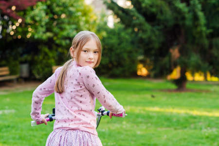 Little sweet girl on her bicycle in a park looking back over her shoulderの写真素材