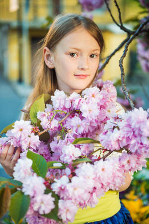 Spring portrait of a cute little girl playing at sunset with flowers of japanese cherry in blossomの写真素材