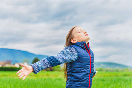 Adorable little girl playing in field with the wind arms open wideの写真素材