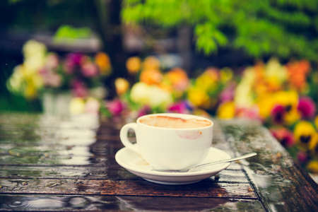 Empty cup of coffee with traces of lipstick on the table under the rain outdoors toned imageの写真素材