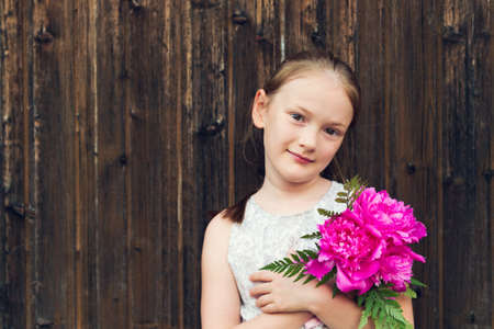 Close up portrait of a cute little girl with beautiful pink peoniesの写真素材