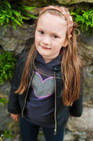 Outdoor portrait of a cute little girl of 5 years old, wearing black leather coatの写真素材