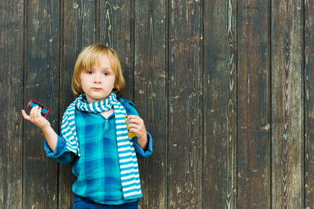 Fashion portrait of a cute little blond  boy against wooden background, wearing emerald shirt and scarfの写真素材
