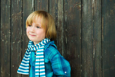 Fashion portrait of a cute little blond  boy against wooden background, wearing emerald shirt and scarfの写真素材