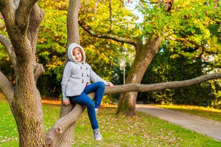 Autumn portrait of a cute little girl playing on a tree in a beautiful park on a nice sunny dayの写真素材
