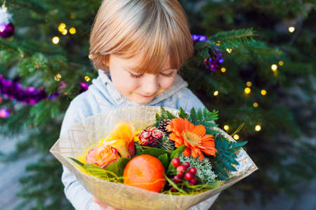Portrait of a cute little boy holding christmas flower bouquet, standing next to christmas treeの写真素材