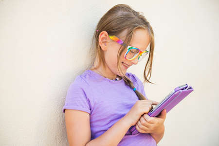 Adorable little girl playing on a digital tablet, wearing rainbow glasses
