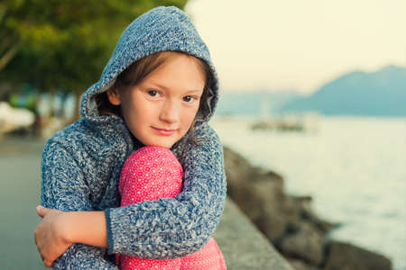 Close up portrait of a cute little girl of 8 years old at sunset, resting by the lakeの写真素材