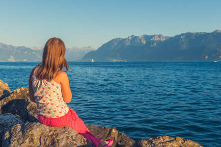 Outdoor portrait of a cute little girl resting by the lake Geneva at sunset, back viewの写真素材