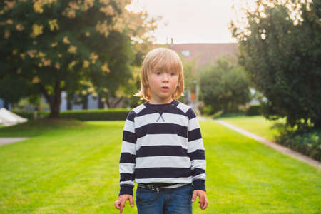 Outdoor portrait of a cute blond child playing on a backyard at sunset, wearing navy stripe topの写真素材