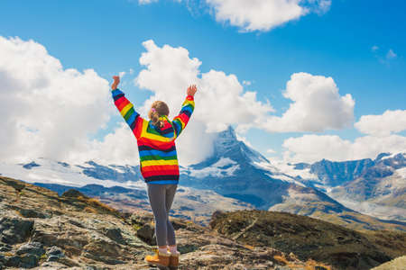 Cute little girl with arms wide open, wearing colorful coat, standing in front of Matterhorn...