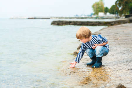 Cute toddler boy having fun outdoors, playing next to lake on a rainy dayの写真素材