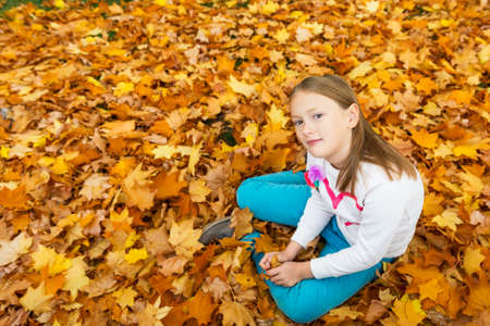Autumn portrait of a cute little girl of 8 years old, playing with yellow leaves in the parkの写真素材