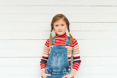 Fashion portrait of a cute little girl against white background, wearing stripe roll neck pullover and denim overallsの写真素材
