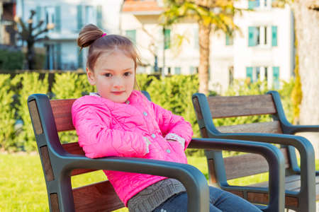 Little girl resting in the park on a nice sunny spring day, wearing bright pink jacketの写真素材
