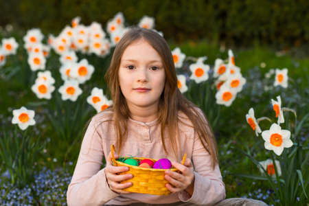 Outdoor portrait of a cute little girl in a spring garden, holding small bascket with colorful easter eggsの写真素材