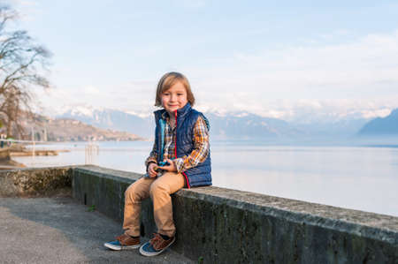 Outdoor portrait of a cute fashion little boy of 4 years old, wearing blue waistcoat, plaid shirt, beige trousers and sneakersの写真素材