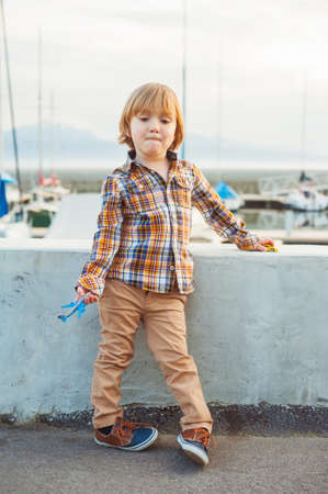 Outdoor portrait of a cute fashion little boy of 4 years old, wearing yellow plaid shirt, beige trousers and sneakersの写真素材