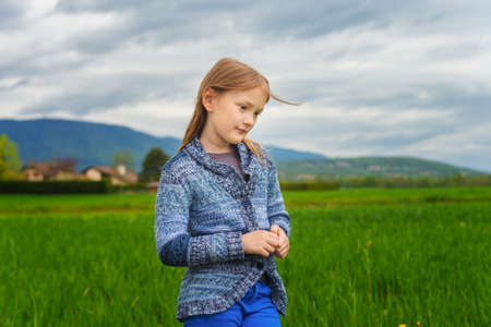 Fashion portrait of cute little girl of 7 years old, wearing blue trousers and knitted jacketの写真素材