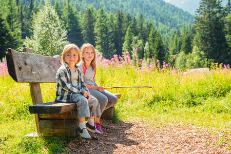 Cute little boy and his sister with backpack hiking in mountains, resting on a benchの写真素材