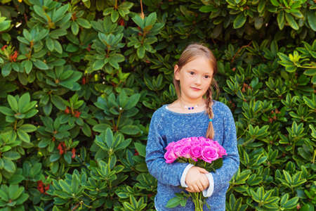 Outdoor portrait of adorable little girl of 7-8 years old, holding beautiful bouquet of bright pink rosesの写真素材