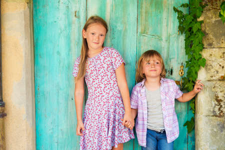 Summer portrait of two cute kids, young girl and her little brother standing against turquoise wooden old doorの写真素材